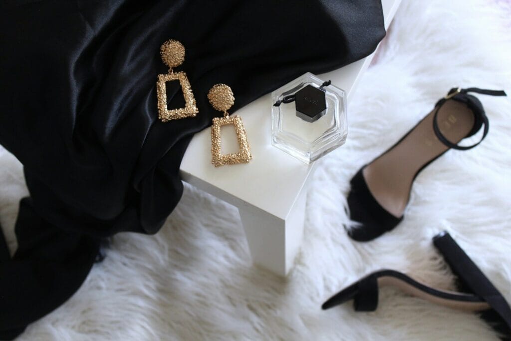 Pair of gold-colored earrings on table and black ankle-strap pumps on area rug